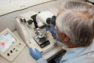 Older male scientist using a microscope to analyze the structure of a particle.